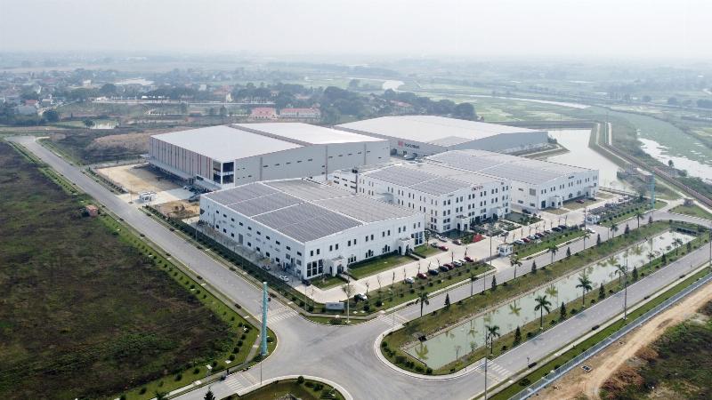 Một khu công nghiệp hiện đại với các tấm pin năng lượng mặt trời trên mái nhà xưởng và cây xanh được trồng xung quanh, thể hiện mô hình công nghiệp hóa xanh và bền vững.